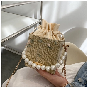 Détail d'un sac seau en paille beige avec broderie florale et anse en perles