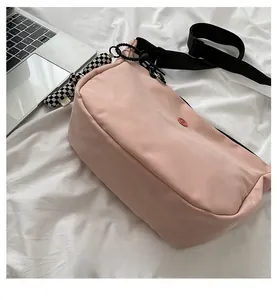 Détail du sac bandoulière en toile rose avec sangle noire et breloque en damier noir et blanc