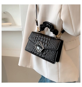 Détail d'un sac à main noir motif crocodile avec poignée plissée et fermoir en métal doré