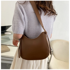 Brown half-moon crossbody bag with wide adjustable strap worn by a model in soft light