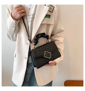Détail d'un sac bandoulière noir matelassé avec boucle dorée et poignée plissée sur modèle