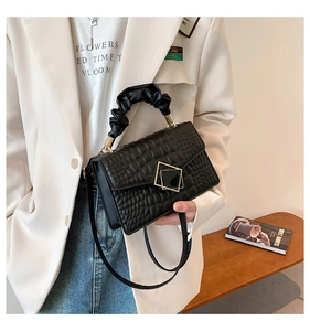 Détail d'un sac bandoulière noir effet crocodile avec poignée plissée et boucle en métal