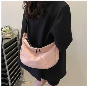 Sac bandoulière rose en forme de croissant porté avec un blazer noir élégant
