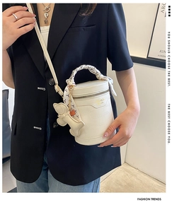Detail of white cylinder bucket bag with crocodile texture, silk scarf handle, and dog charm