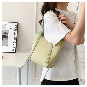 Close-up of pistachio green tote bag with dark green trim held by a model in casual wear