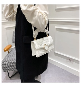 Détail d'un sac blanc à motif crocodile avec fermoir géométrique doré et anse plissée