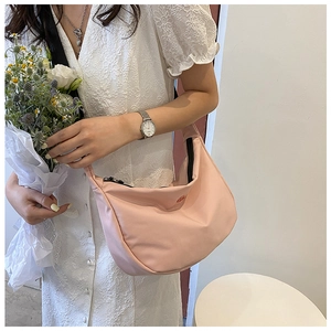 Sac bandoulière demi-lune rose présenté avec une robe en dentelle blanche élégante