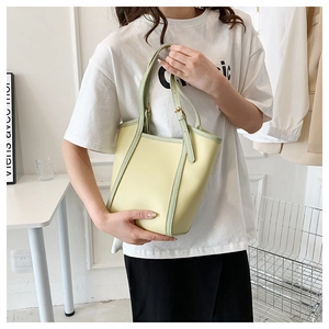 Detail of light yellow tote bag featuring contrast green straps and adjustable buckles