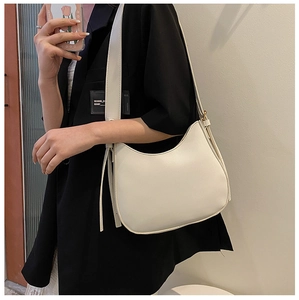 Close-up of minimalist ivory white crescent shoulder bag worn on a black blazer
