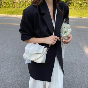 White square crossbody bag with bow decoration and pearl handle shown on shoulder