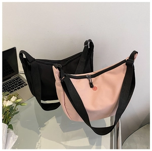 Sacs bandoulière demi-lune en nylon rose et noir avec larges sangles sur table en verre