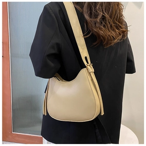 Side view of a beige crescent moon leather shoulder bag worn over a dark blazer