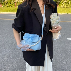 Light blue crossbody bag with bow and pearl chain shown in a street style look