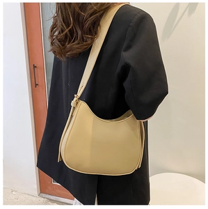 Side view of a beige crescent faux leather shoulder bag worn over a black blazer