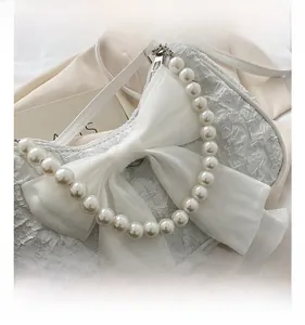 Dettaglio di borsa in tessuto bianco con grande fiocco e manico di perle eleganti