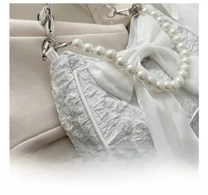 Dettaglio del tessuto jacquard bianco plissettato con fiocco di seta e perle