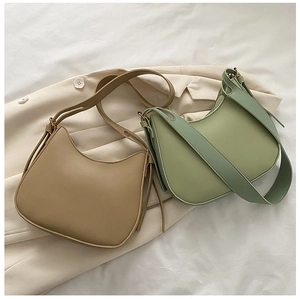 Flat lay of khaki and green crescent crossbody bags with wide straps on white bedding