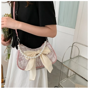 Detail of pink lace pleated handbag with cream bow and pearl handle carried by a model