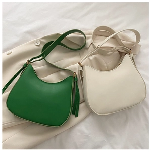 Macro shot of minimalist half-moon crossbody bags in green and cream with golden hardware