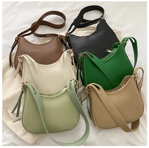 Flat lay of half-moon leather crossbody bags in six vibrant colors on white fabric