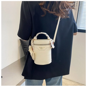 Detail of cream bucket bag with crocodile texture, scarf-wrapped handle and bow charm