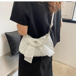 Borsa a mano bianca a pieghe con fiocco e manico di perle indossata da una modella in posa