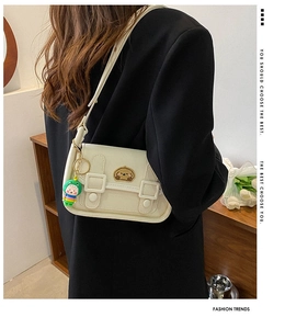 Detail view of cream-white shoulder bag with cartoon dog patch and dinosaur doll pendant