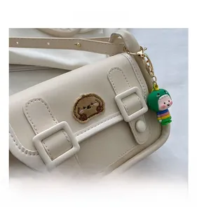 Detail of cream mini crossbody bag featuring a cute brown bear patch and dinosaur charm