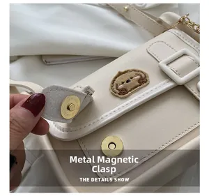 Detail of metal magnetic buckle and dog embroidery on off-white PU leather shoulder bag