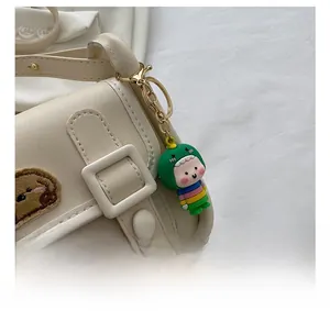 Close-up of a colorful dinosaur bag charm attached to a beige leather shoulder bag
