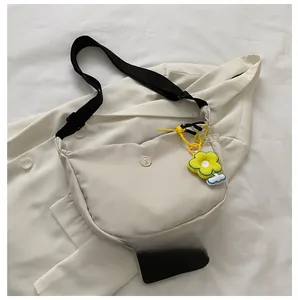 Size comparison of a beige nylon crossbody bag with a yellow flower charm and smartphone