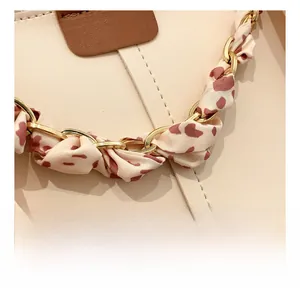 Detailed close-up of golden chain hardware and silk ribbon on beige leather handbag
