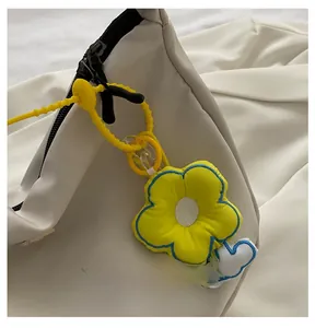 Detail of yellow flower bag charm with blue stitching on a white minimalist fabric bag