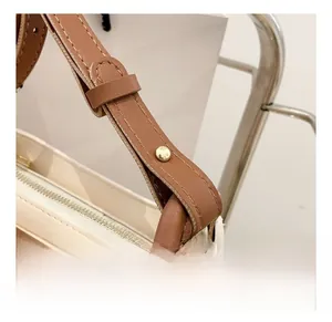 Detailed view of dark brown leather strap with golden metal link and cream white bag body