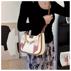 Detail of a chic bucket bag with gold chain and floral scarf accessory worn by a model