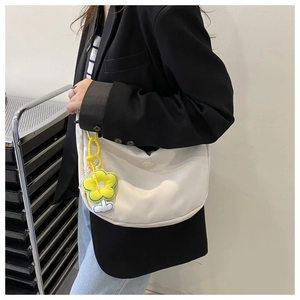 White crescent crossbody bag detail with yellow flower charm worn by a model in casual setting