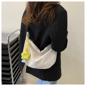 White crescent canvas crossbody bag with sunflower charm shown on model shoulder
