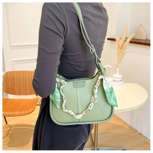 Close-up of mint green leather shoulder bag with decorative floral silk scarf and gold chain