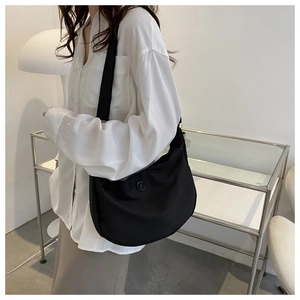 Side view of a minimalist black crescent nylon crossbody bag on a model in a modern room