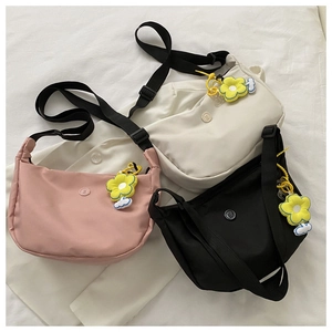 Three minimalist nylon crossbody bags in pink, beige, and black with sunflower charms