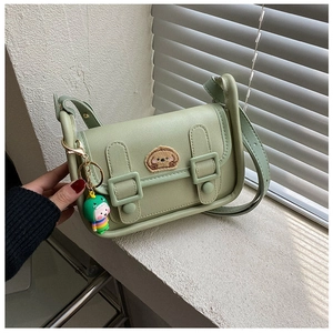 Detail of light green crossbody bag with bear patch and dinosaur keychain accessory