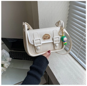 Detail view of a cream crossbody bag with bear embroidery and green dinosaur charm