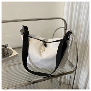 Detail shot of the white crossbody bag featuring a round B logo and black nylon shoulder strap