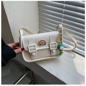Detail of cream crossbody bag featuring a cute bear patch and dinosaur keychain