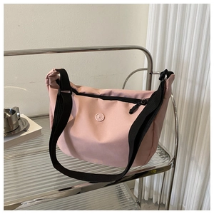 Detailed view of pink nylon crossbody bag with black adjustable strap and circular logo