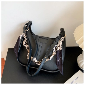 Detail of black leather crossbody bucket bag featuring decorative silk scarf and gold chain