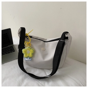 White nylon dumpling bag with black strap and yellow sunflower charm by a laptop