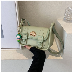 Detail of mint green crossbody bag with cartoon dog embroidery and colorful doll pendant