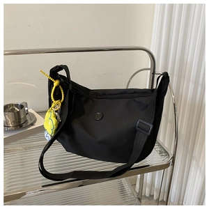 Detail of black nylon crossbody bag featuring a yellow flower charm on a modern shelf