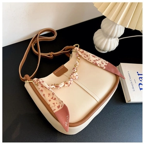Detail of a beige half-moon shoulder bag featuring a silk scarf-wrapped handle design